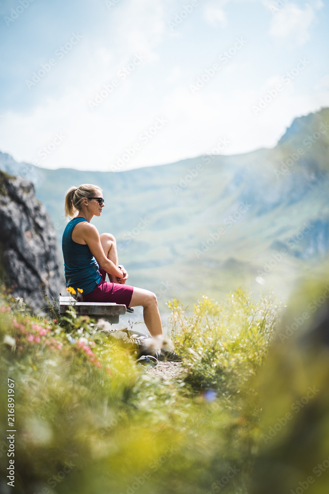Beautiful Sportive Hiker girl having a break and relaxing on a bench near a lake enjoying the sunshine