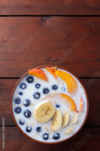 Oatmeal porridge with milk and fruit on a wooden background, healthy porridge with pieces of banana and peach, breakfast with fiber, calcium and vitamins, food for the schoolboy