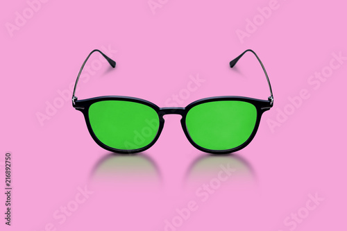 Elegant glasses made of dark plastic and metal, with green glasses on a pink background