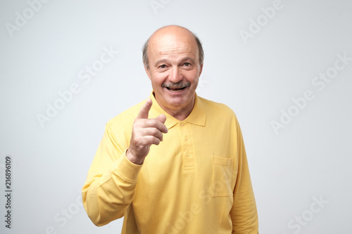 Portrait of attractive senior man pointing with forefingers at you, smiles broadly with teeth photo