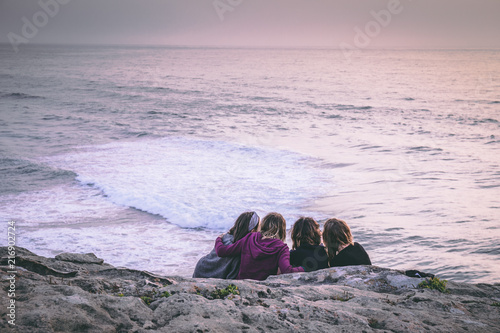 A group of girlfriends watch the sun set while siting down near a cliff in Monte Clerigo, Portugal