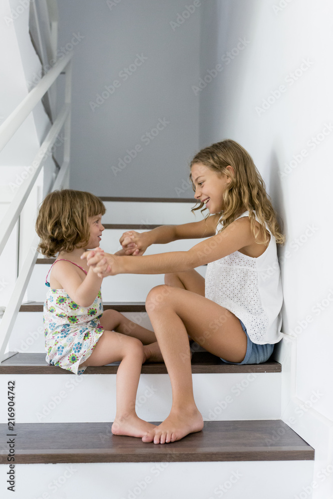 Portrait of two happy children sitting on the stairs in the house. The concept sisters forever. Fun indoors. Family lifestyle Portrait of two happy children sitting on the stairs in the house. The concept sisters forever. Fun indoors. Family lifestyle