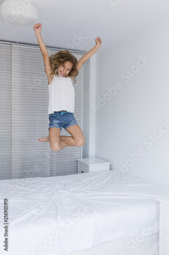 beautiful kid girl playing and jumping on bed. Fun indoors. Family love and lifestyle