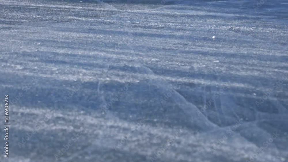 Snow is flying over surface of ice. Snowflakes fly on ice of Lake Baikal. Ice is very beautiful with unusual unique cracks. Snow sparkles and glows in red. Shooting slow motion 180fps. Picture at Snow is flying over surface of ice. Snowflakes fly on ice of Lake Baikal. Ice is very beautiful with unusual unique cracks. Snow sparkles and glows in red. Shooting slow motion 180fps. Picture at