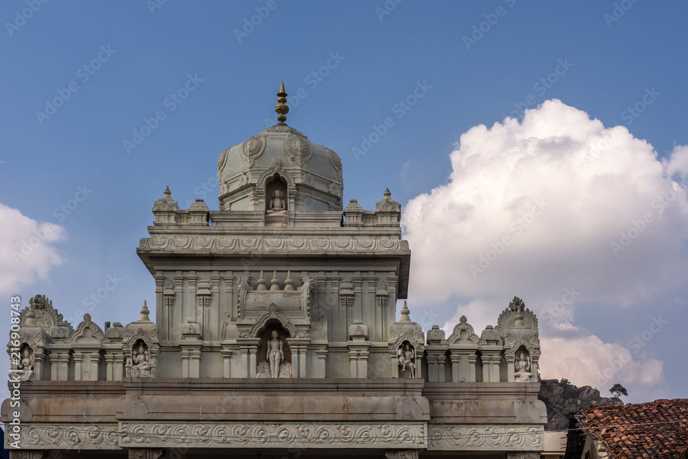 Shravanabelagola, Karnataka, India - November 1, 2013: Gray cement upper structure of gate into the Jain sanctuary features dome and small statues under blue sky with white cloud.