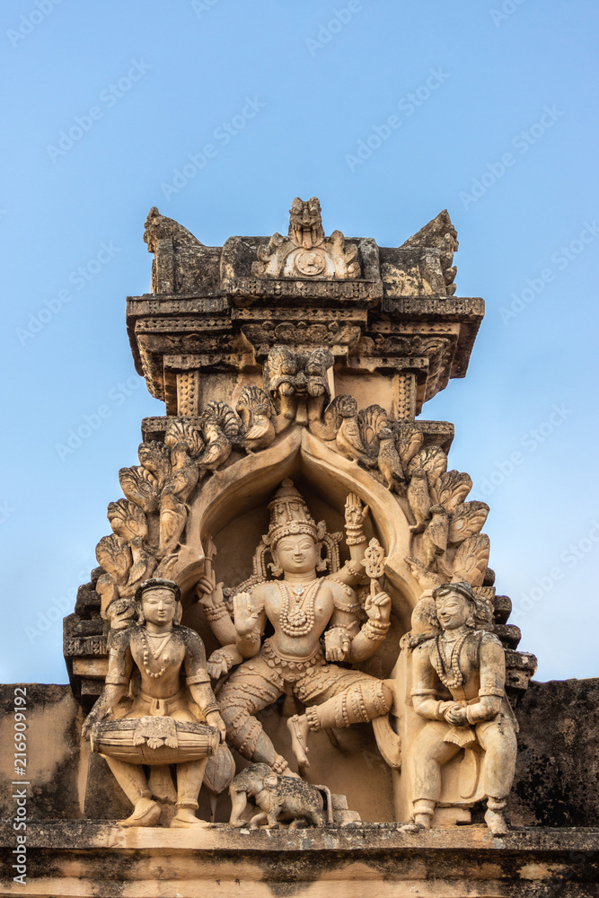 Shravanabelagola, Karnataka, India - November 1, 2013: Brown stone with black mold deity statue in niches on edge of roof at Jain Tirth building. Dancing Shiva with elephant and two musicians. Shravanabelagola, Karnataka, India - November 1, 2013: Brown stone with black mold deity statue in niches on edge of roof at Jain Tirth building. Dancing Shiva with elephant and two musicians.