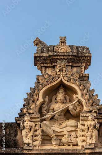 Shravanabelagola, Karnataka, India - November 1, 2013: Brown stone with black mold deity statue in niches on edge of roof at Jain Tirth building. Saraswati goddess with instrument.