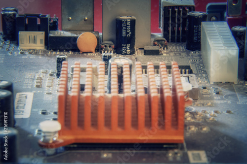 A landscape made of computer components on a motherboard, focus on an orange dissipator. Above macro shot.
 photo