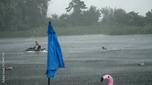summer rain, thunderstorm, heavy rainfall on an empty beach, lonely beach umbrellas are standing, strong, gusty wind, on the river slowly swims Water bike, fell into a shower. photo