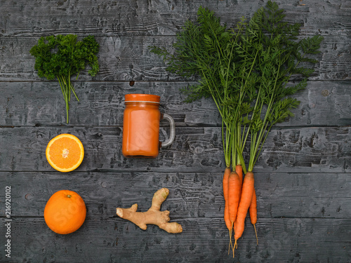 Freshly made carrot smoothie, bunch of carrots, orange and ginger root on a rustic table. The view from the top. Flat lay. photo