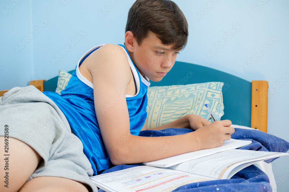 Teen boy doing homework on his bed Teen boy doing homework on his bed