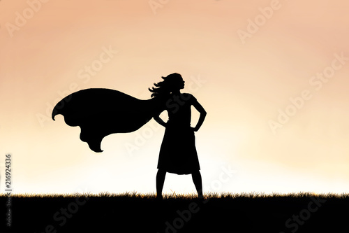 Strong Beautiful Caped SuperHero Woman Silhouette Isolated Against Sunset Sky Background