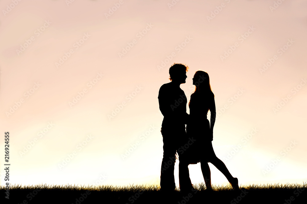 Happy Young Couple in Love Silhouetted Against Sunset in the Sky