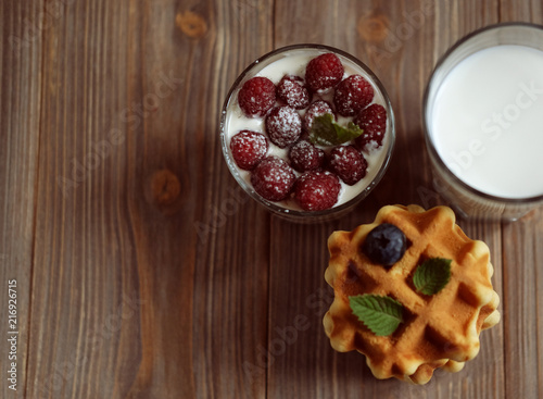 Good breakfast. Belgian waffles with blueberries, a glass of milk and granola with raspberries over wooden table.