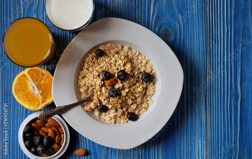 Healthy eating, food and diet concept - tasty oatmeal with berries and glass of orange juice. Top view. Blue wooden background.