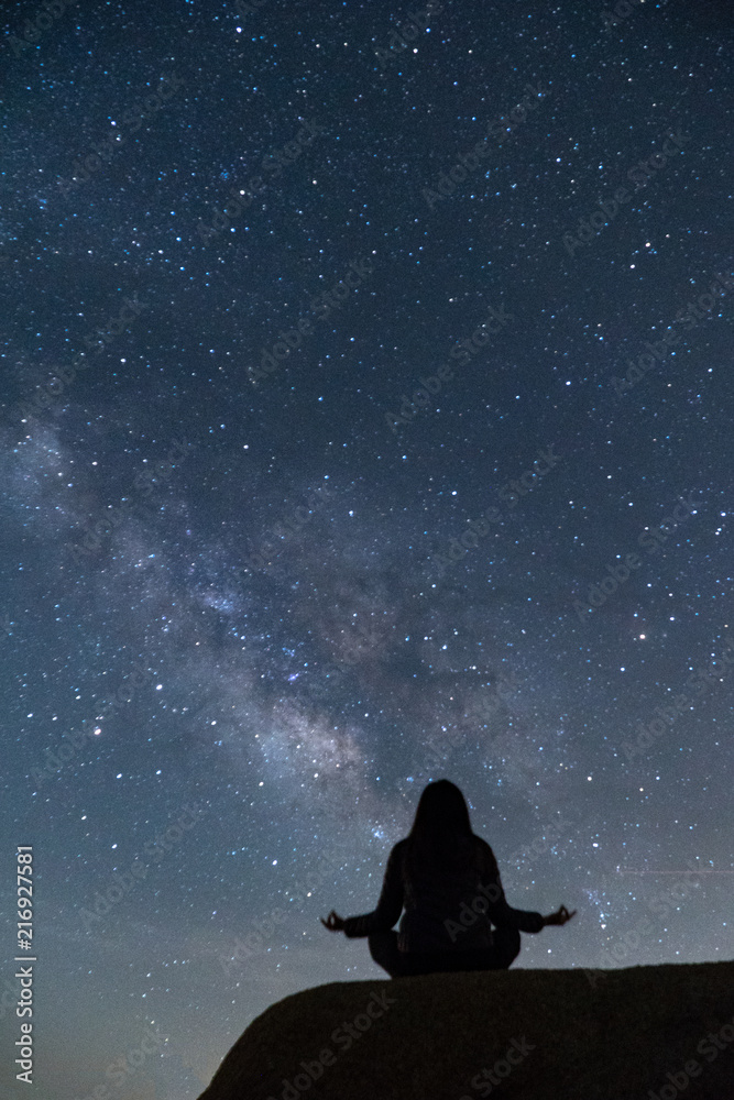 Girl meditating in lotus pose under the beautiful Milky Way night sky