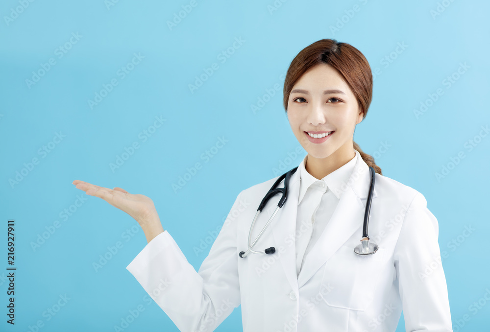 Smiling female doctor pointing with finger on blue background Smiling female doctor pointing with finger on blue background