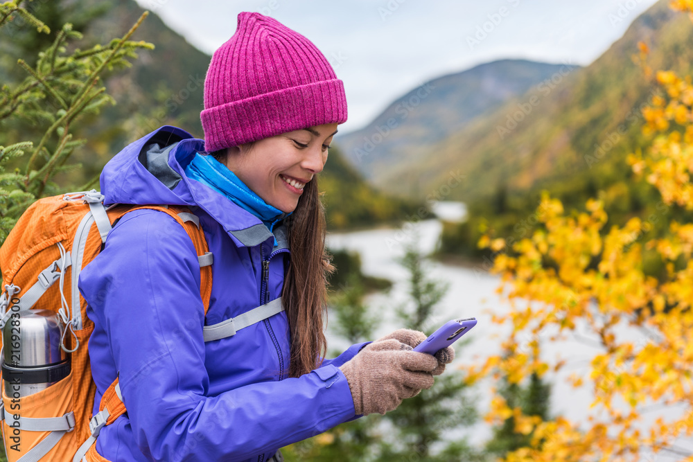 Mobile young girl using technology in autumn hiking outdoor. Happy Asian woman playing smartphone games outside Mobile young girl using technology in autumn hiking outdoor. Happy Asian woman playing smartphone games outside