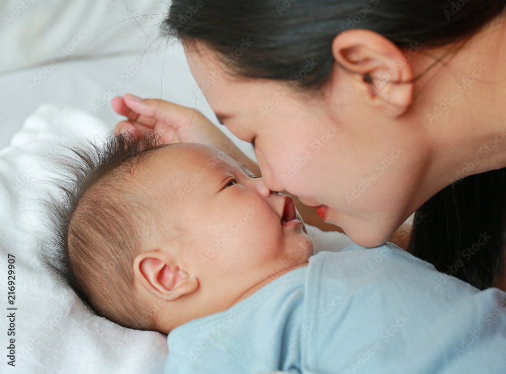 Close up mother kissing baby boy lying on the bed. - obrazy, fototapety, plakaty 