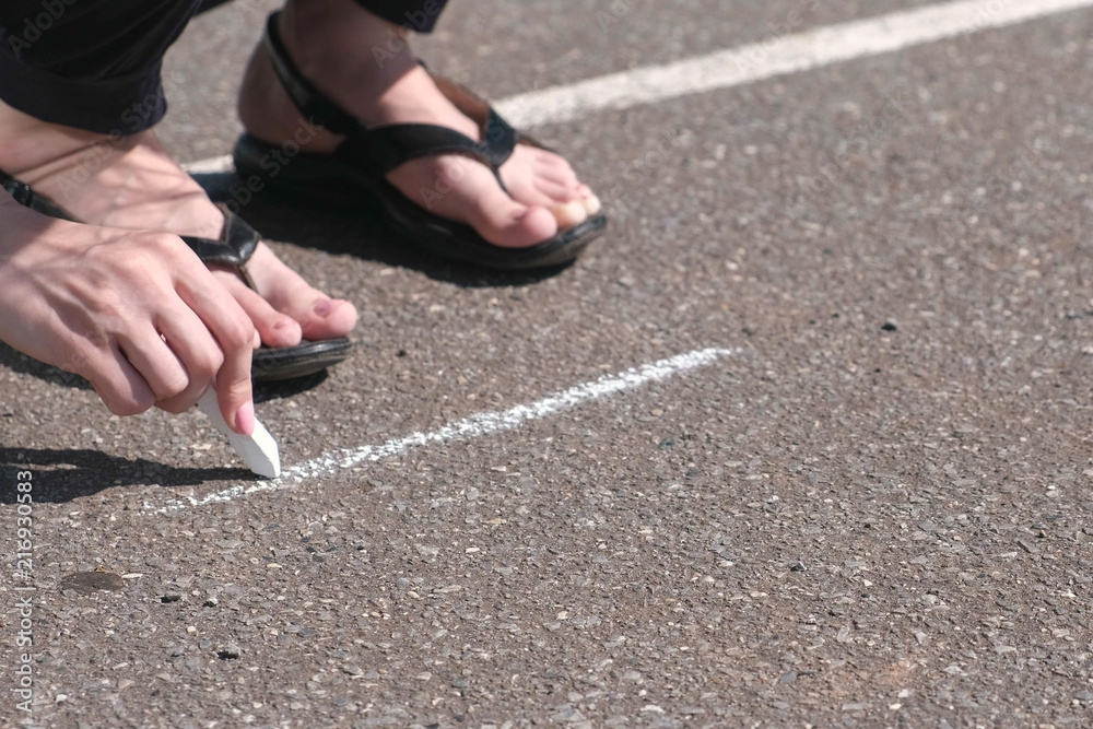 Woman draws a square on the asphalt with white chalk. Close-up hands.