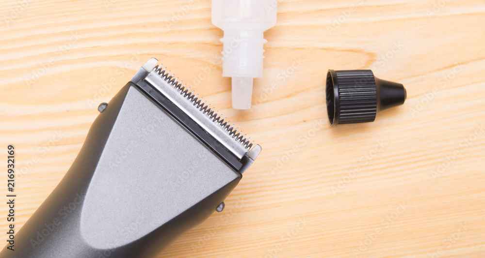 on a light wooden background, lies an electric machine for shaving hair and oil for lubricating blades. on a light wooden background, lies an electric machine for shaving hair and oil for lubricating blades.