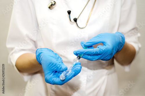 a nurse in a white coat and blue gloves holds an ampoule with medicine in her hands and a syringe for administering the medicine to the patient