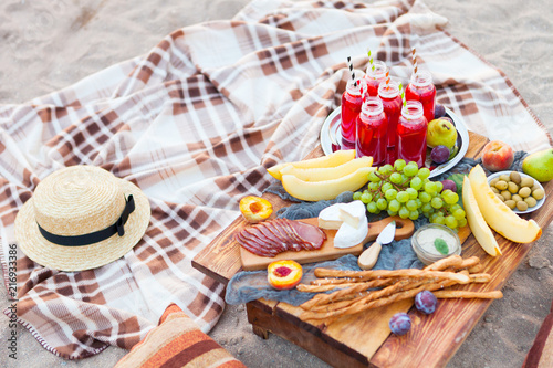 Picnic on the beach at sunset in the style of boho. Concept outdoors evening healthy dinnner with fruit and juice