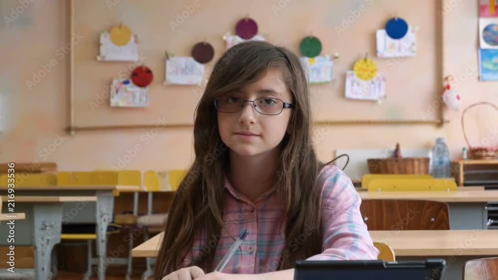 Teenage girl in glasses- high school student smiles to camera seated in classroom Teenage girl in glasses- high school student smiles to camera seated in classroom