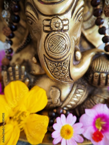 Hindu God Ganesha is covered with coloured flowers on an altar for a spiritual ceremony 