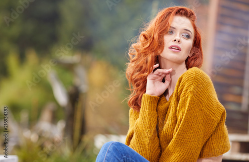 Autumn woman relaxing on a wooden terrace in the morning. Female model with redhair