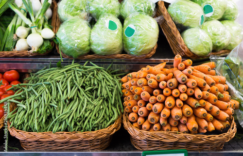 Green beans and carrots in wicker baskets on counter of vegetable store photo