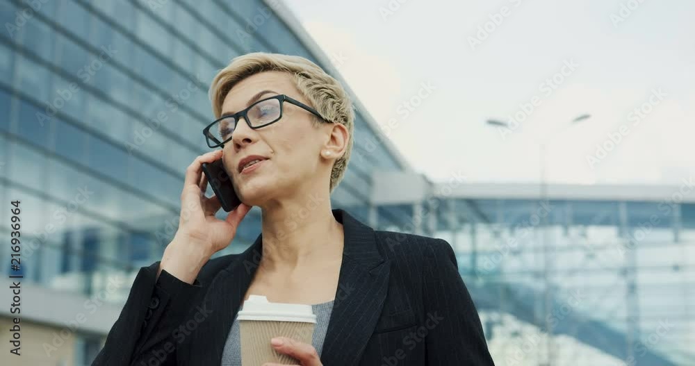 Close up odf the beautiful Caucasian woman office worker talking on the phone while drinking her morning coffee near the office building. Close up odf the beautiful Caucasian woman office worker talking on the phone while drinking her morning coffee near the office building.