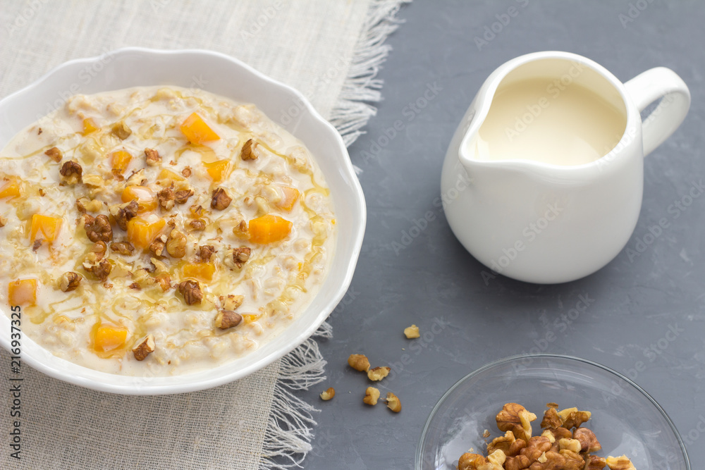 Pumpkin oatmeal with honey and nuts, milk in a milkman, walnuts on a gray background. healthy delicious homemade breakfast Pumpkin oatmeal with honey and nuts, milk in a milkman, walnuts on a gray background. healthy delicious homemade breakfast