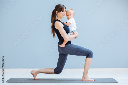 Sport, motherhood and active lifestyle concept - side view of young mother doing yoga with toddler baby at home. Lounge exercise.