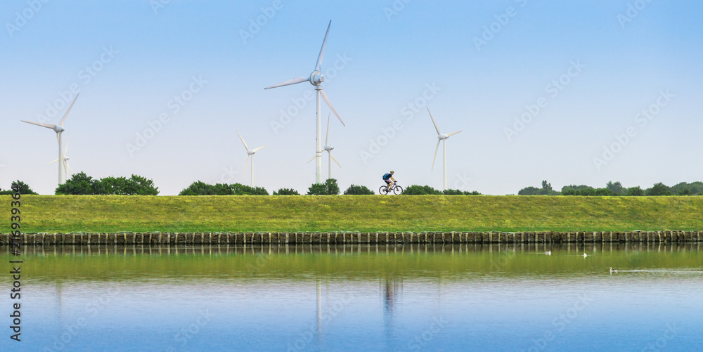 Cyclist drives on the dike. Nearby are wind turbines	