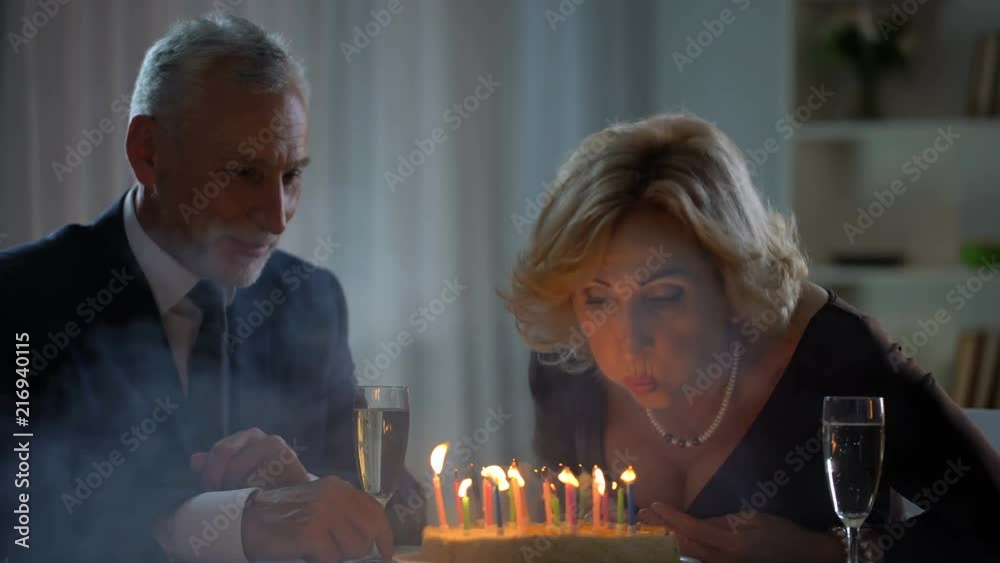 Elderly wife blowing cake candles, drinking champagne with husband, tradition