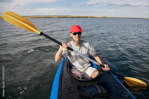  A man on a kayak floats on the lake. Sports on the water. The athlete is holding an oar.