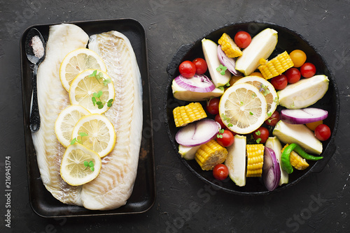 Two dishes before baking: cod with lemons and assorted organic garden vegetables in round form: corn, zucchini, onion, tomatoes, herbs. Top View. photo