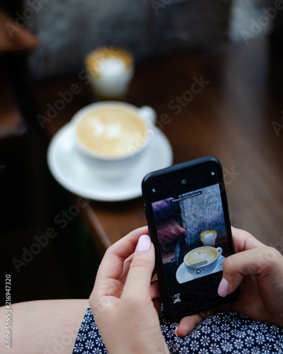 The girl is taking pictures of coffee on a smartphone. Hands with the phone close-up pictures of food.