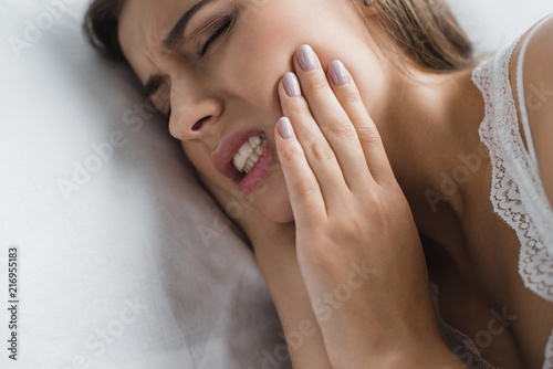 close-up view of young woman suffering from toothache while lying in bed photo