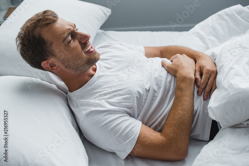 high angle view of man lying in bed and suffering from stomach ache
