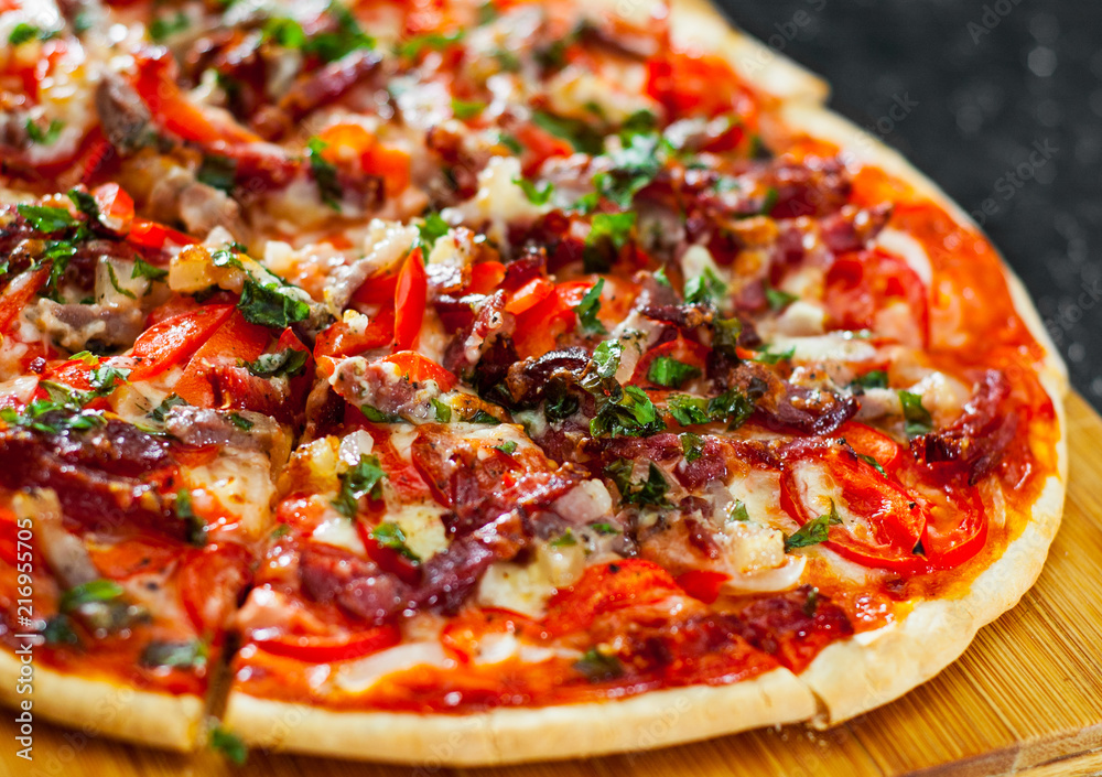 sliced Pizza with Mozzarella cheese, Ham, Tomatoes, salami, pepper, bacon, pepperoni, Spices and Fresh Basil. Italian pizza