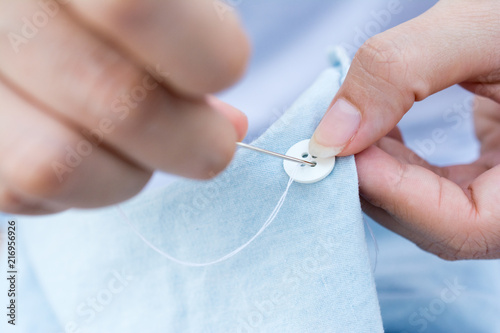 Hands of a woman sew a button with a needle close up. Woman is sewing buttons a shirt.