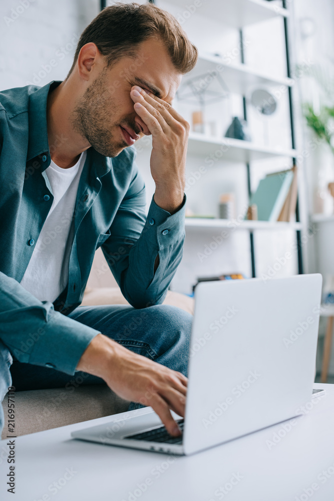 young man with pain in eyes and headache using laptop at home young man with pain in eyes and headache using laptop at home