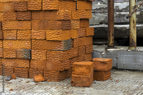 stack of bricks made of red clay on the background of some structures of a building under construction