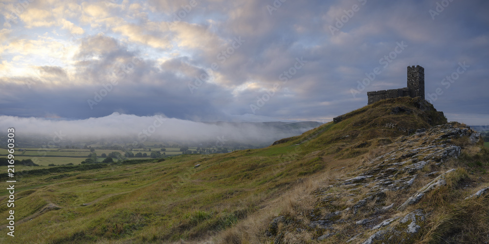 Summer sunrise on Brentor showning St Michael's church atop the tor with dramatic weather clouds of showers and mist, on the western edge of the Dartmoor National Park. UK Summer sunrise on Brentor showning St Michael's church atop the tor with dramatic weather clouds of showers and mist, on the western edge of the Dartmoor National Park. UK