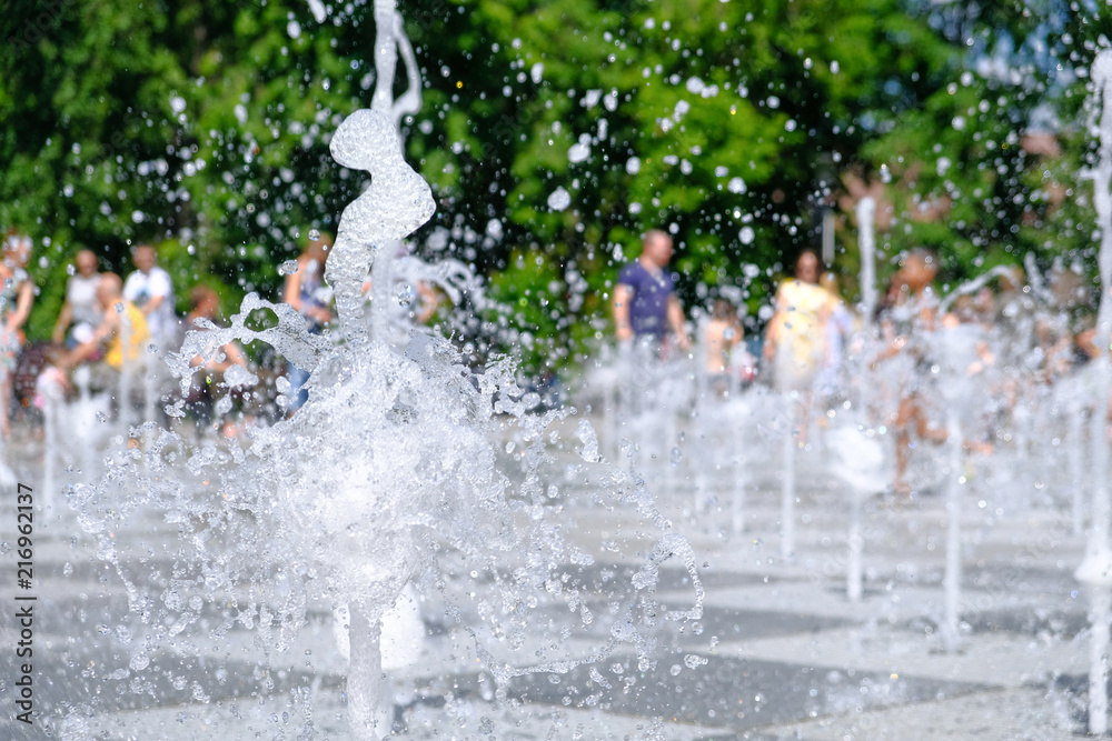 Summer fountain with splashes in a city park with blurred people.