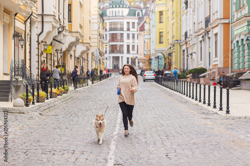 The woman running with husky dog at sunny autumn day on old European city street. Horizontal view photo