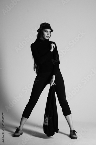 girl in a black suit with a hat, hair posing in the Studio on a gray background. black and white photo