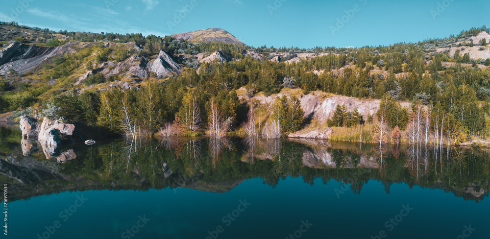 Aerial drone photo of beautiful shore reflecting in water,view inside abandoned quarry, the slopes overgrown of mixed forest, Russia